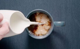  Adding cream to a blue cup on a table. Milk coffee. Dark blue.